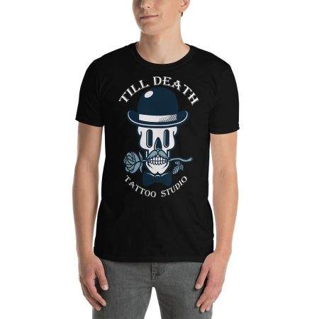 A person wearing the unisex basic softstyle black T-shirt showcases a bold graphic of a skull in a bowler hat, smoking a pipe, and holding roses. The short-sleeve shirt is adorned with the text "TILL DEATH TATTOO STUDIO," providing an edgy style ideal for any tattoo lover.