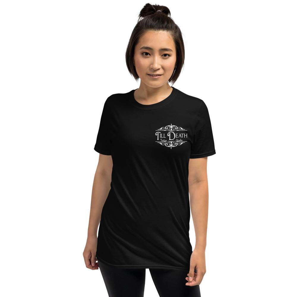 A person wearing the Unisex Basic Softstyle T-Shirt in black, featuring "Till Death" on the front, stands against a plain white background, exuding an edgy vibe reminiscent of a tattoo studio T-shirt.