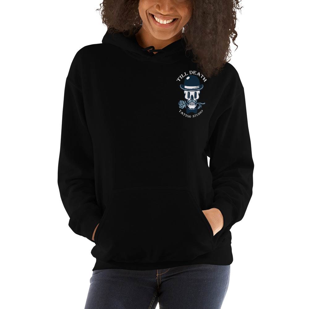 A person is smiling with hands in pockets while wearing the unisex-heavy-blend-hoodie-black-front-602569a74d416.jpg, which features a skull and crossbones design.