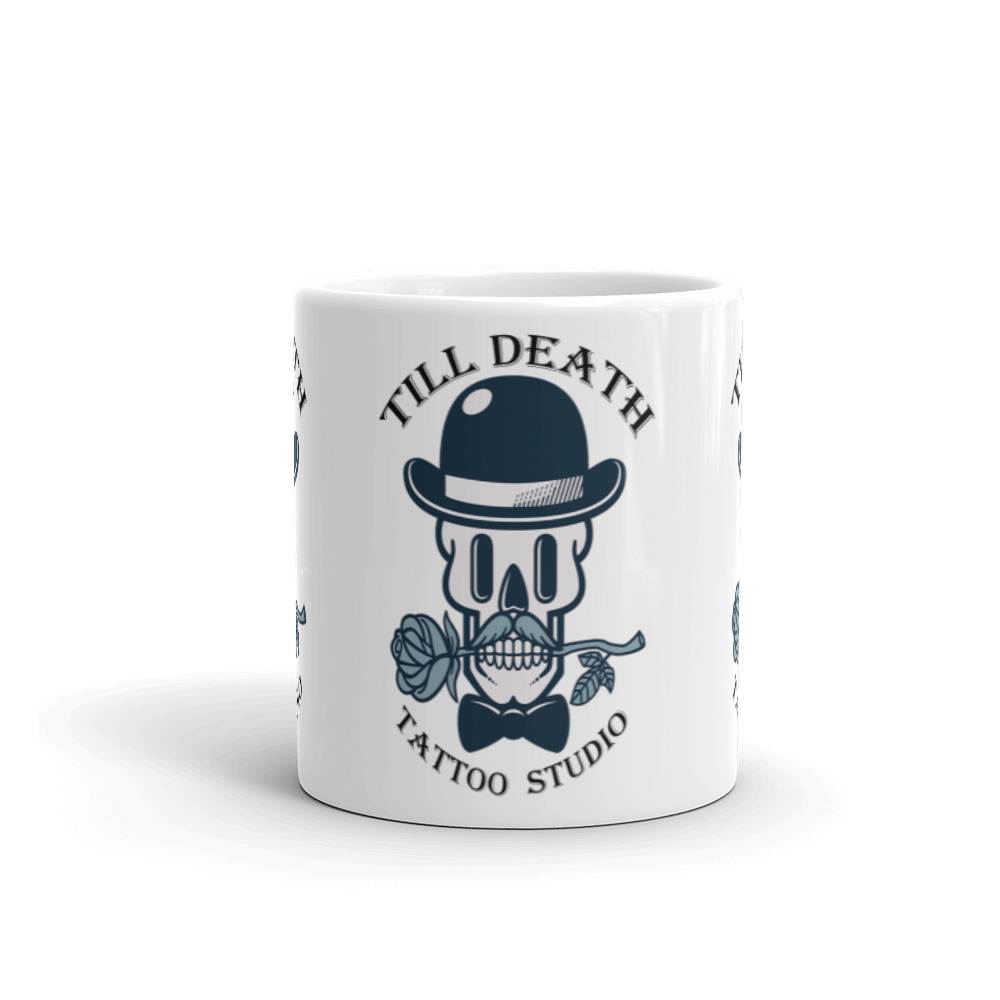 Introducing our white glossy mug, featuring a striking skull adorned with a bowler hat and bow tie, gripping a rose between its teeth. The phrase "Till Death" graces the top while "Tattoo Studio" is elegantly placed below, adding an edgy flair to your morning coffee ritual.