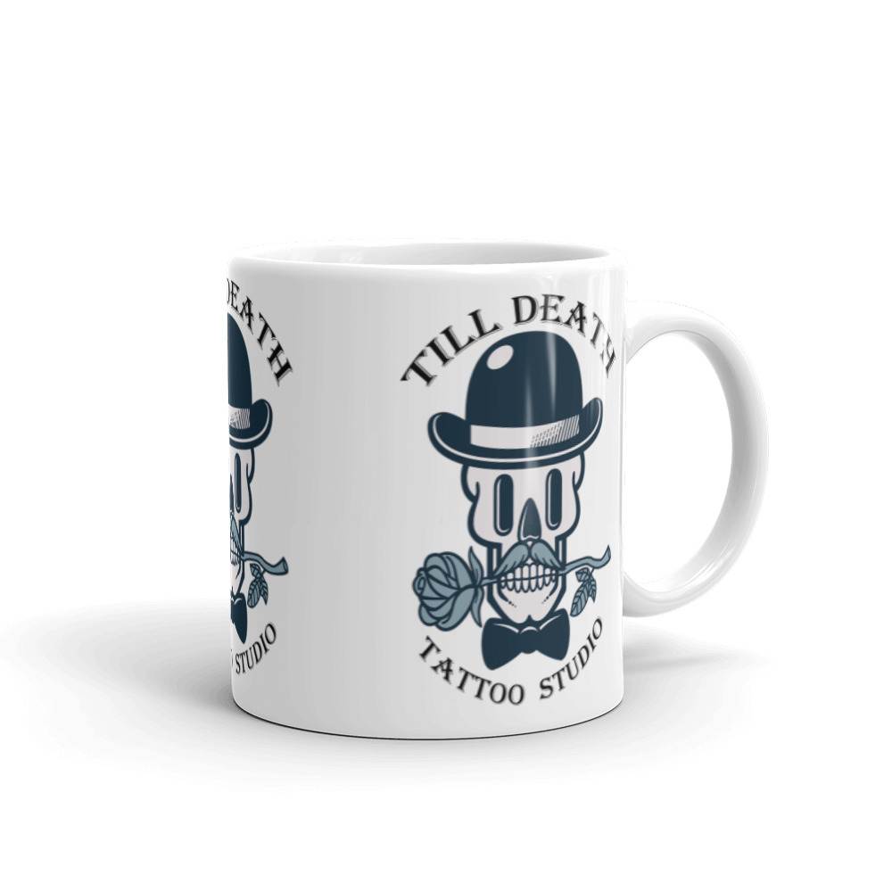 White glossy coffee mug (11oz) with the handle on the right, showcasing a black and white design of a skull wearing a bowler hat and holding a rose in its teeth. The text boldly states "Till Death Tattoo Studio.